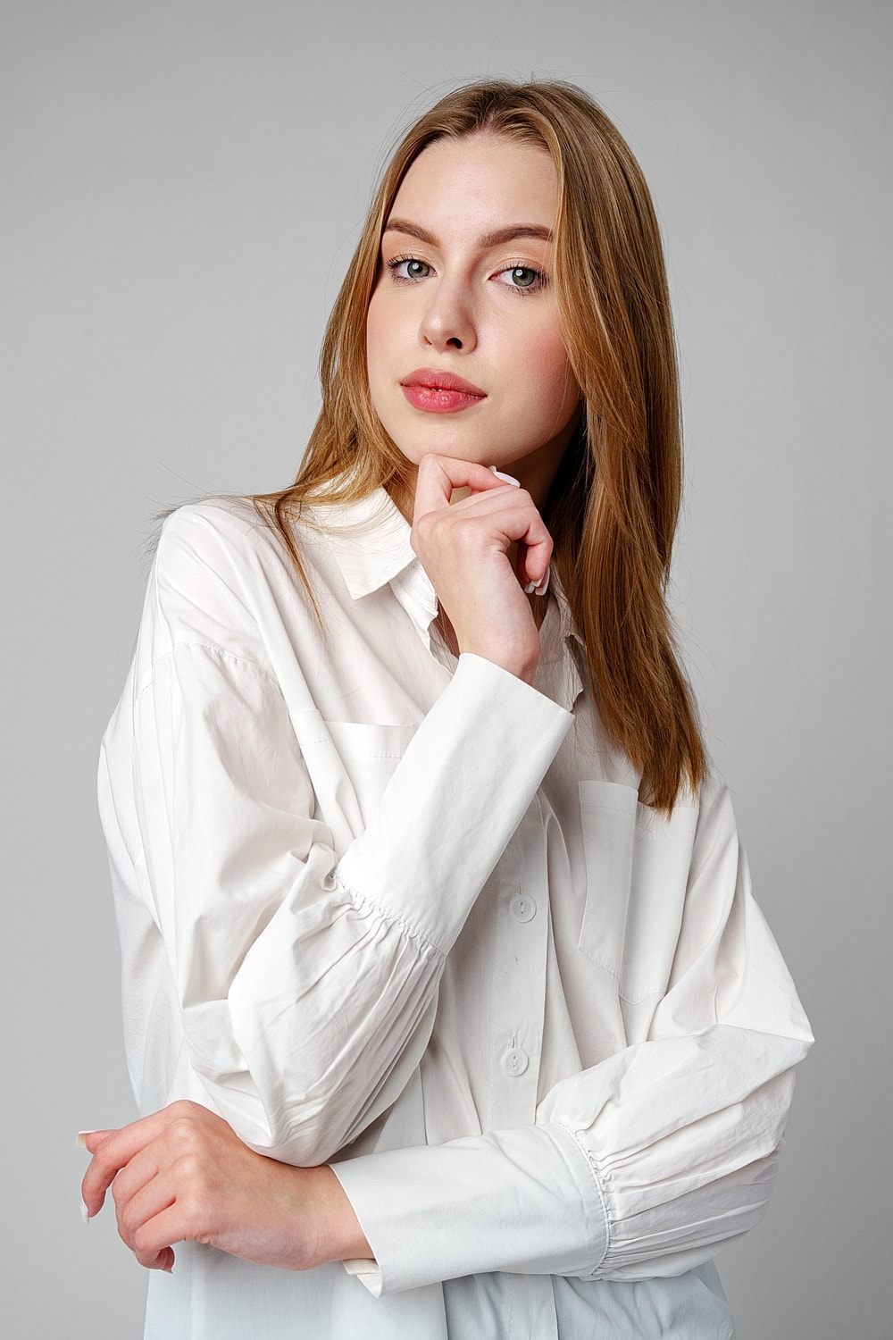 Young woman posing thoughtfully in white shirt.