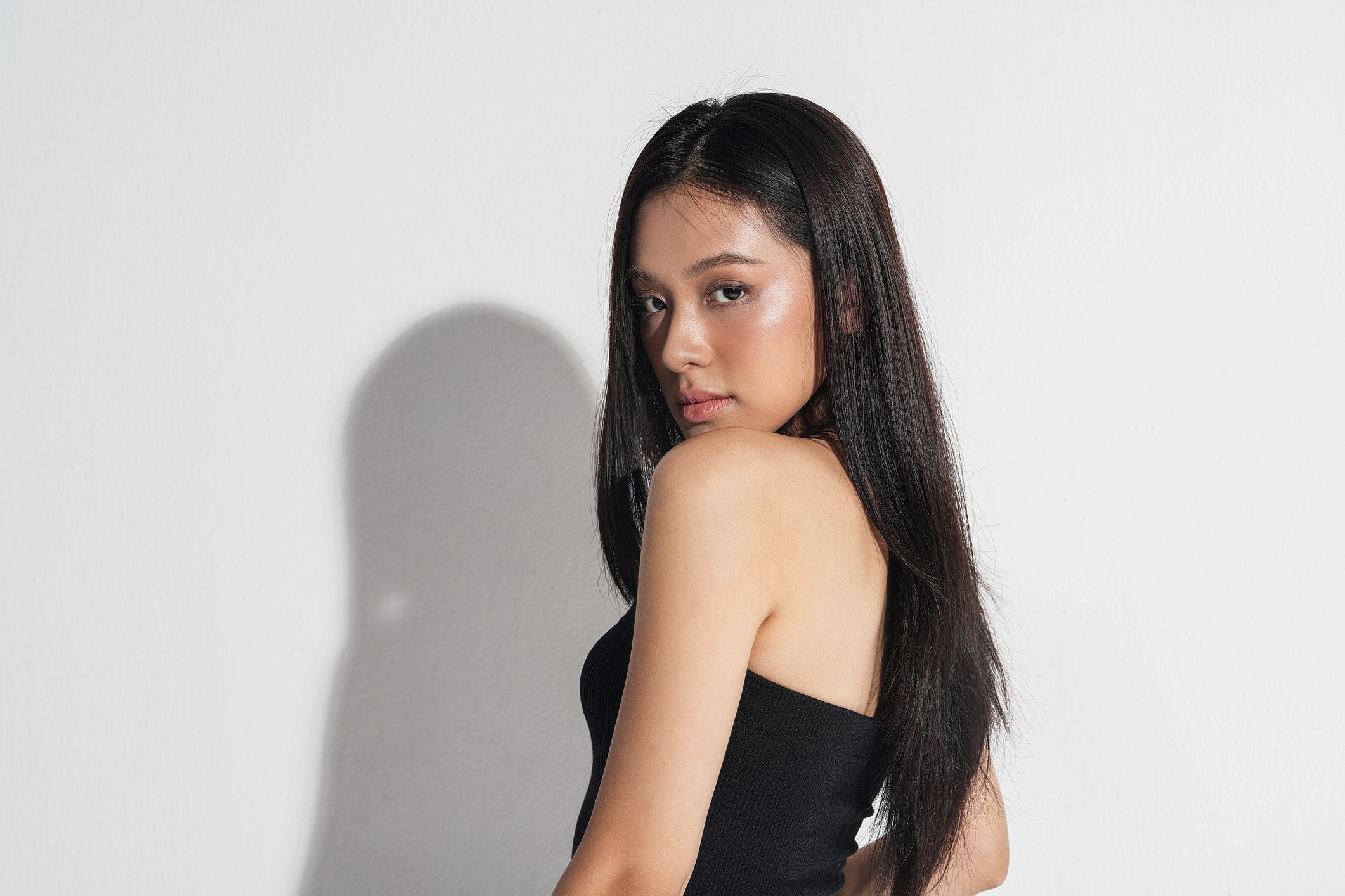 Woman with long hair, posing by white wall.